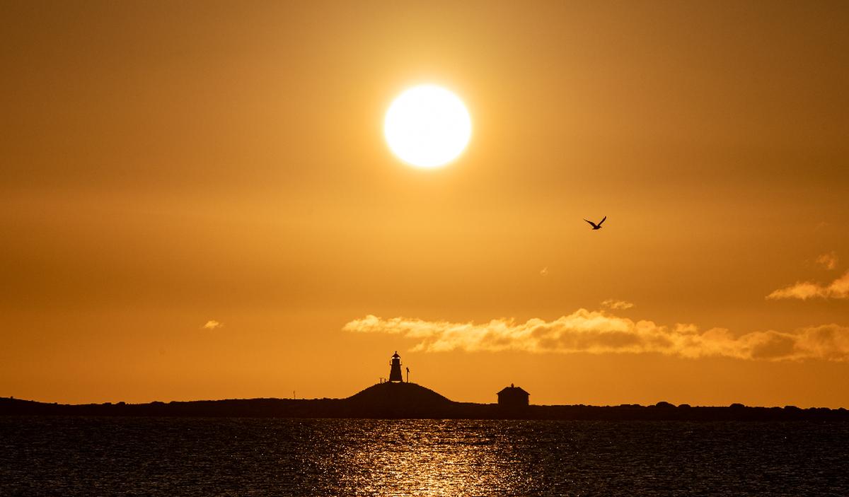 Solnedgang over Lista Fyr med mennesker i silhuett